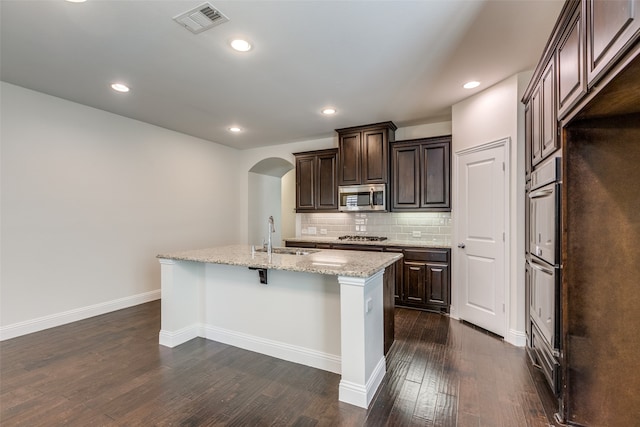 kitchen with dark brown cabinetry, a center island with sink, sink, dark hardwood / wood-style floors, and appliances with stainless steel finishes