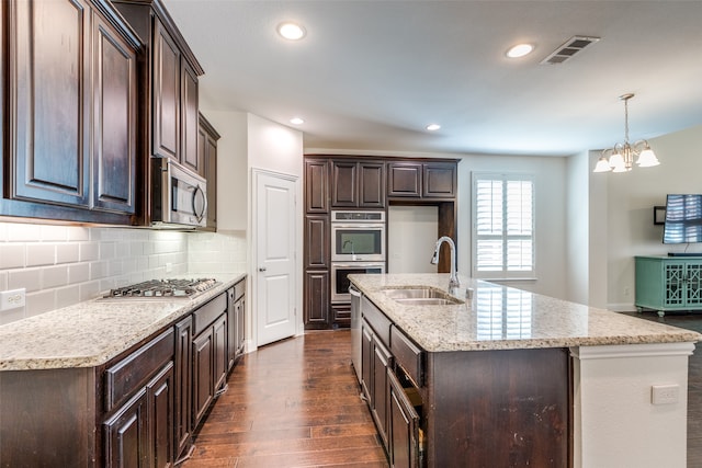 kitchen with appliances with stainless steel finishes, dark hardwood / wood-style flooring, dark brown cabinetry, and an island with sink