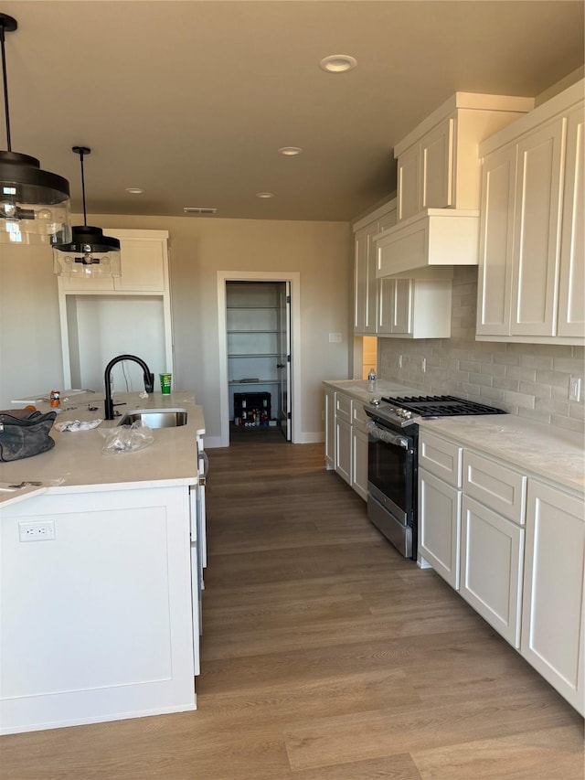 kitchen with sink, hanging light fixtures, stainless steel gas range, light hardwood / wood-style floors, and white cabinets