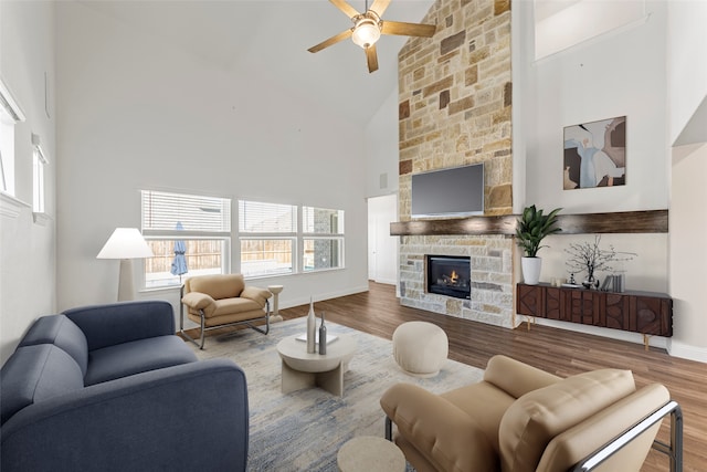 living room featuring high vaulted ceiling, ceiling fan, a stone fireplace, and hardwood / wood-style floors