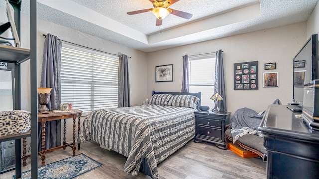 bedroom with a textured ceiling, hardwood / wood-style flooring, a tray ceiling, and ceiling fan