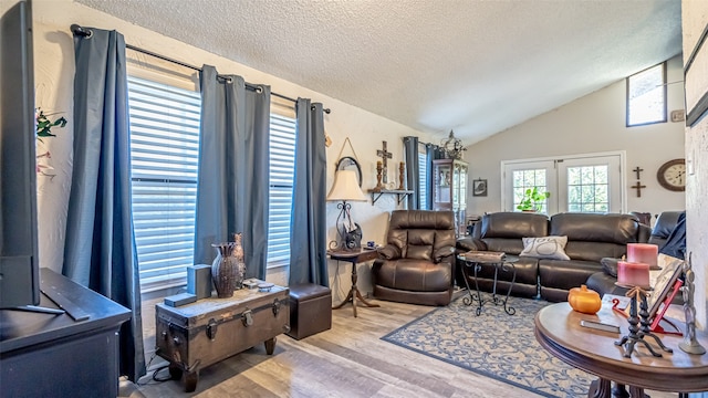 living room with french doors, light hardwood / wood-style floors, a textured ceiling, and lofted ceiling