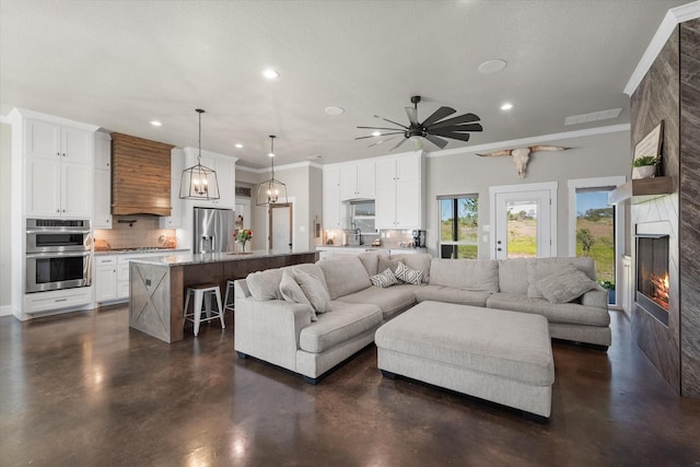 living room with ceiling fan with notable chandelier, sink, a high end fireplace, and crown molding