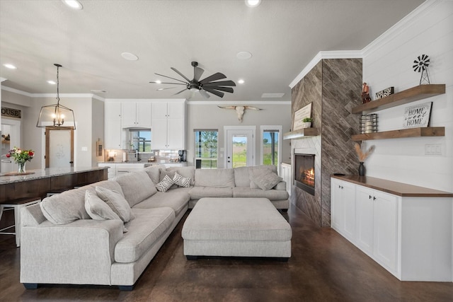 living room with a large fireplace, crown molding, ceiling fan with notable chandelier, and sink