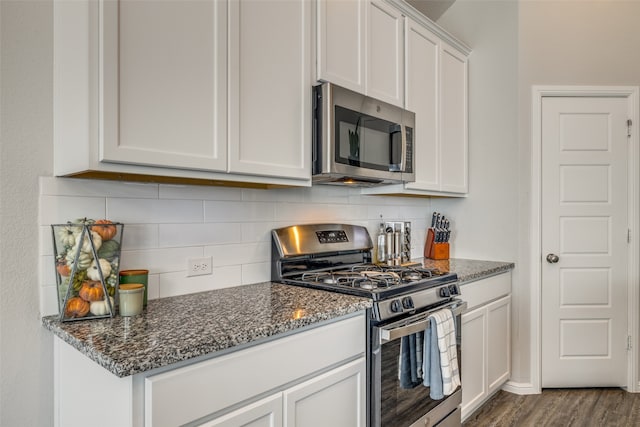 kitchen featuring dark stone countertops, appliances with stainless steel finishes, dark wood-type flooring, decorative backsplash, and white cabinetry