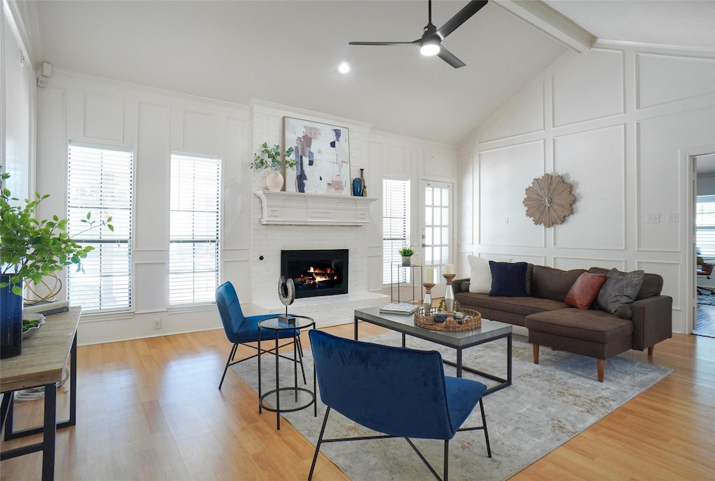 living room with vaulted ceiling with beams, ceiling fan, a fireplace, and light wood-type flooring