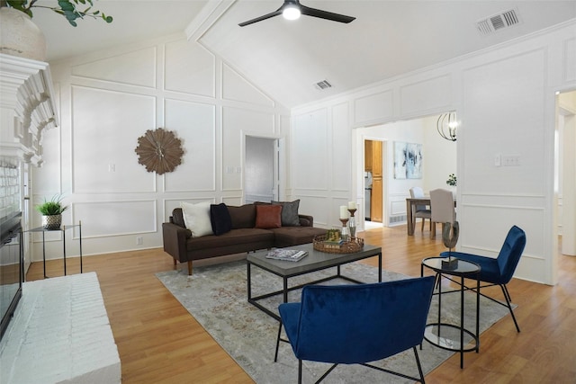 living room with light hardwood / wood-style flooring, a brick fireplace, vaulted ceiling, and ceiling fan