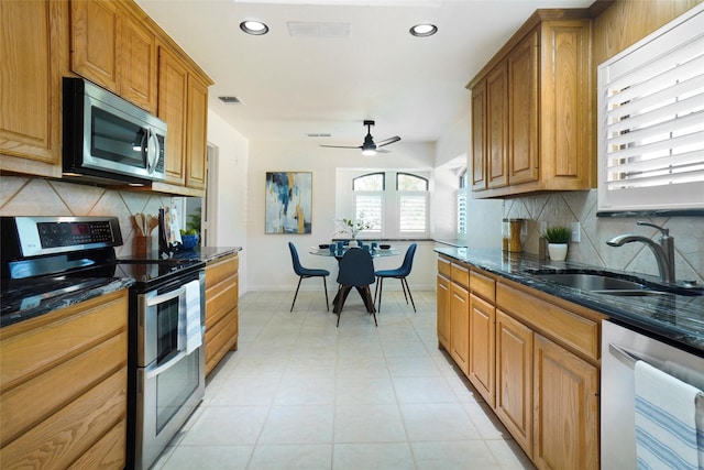 kitchen featuring sink, dark stone countertops, appliances with stainless steel finishes, ceiling fan, and backsplash