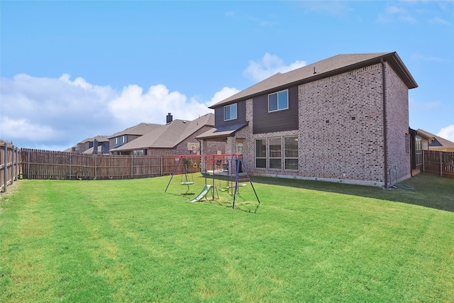 rear view of property featuring brick siding, a fenced backyard, a playground, and a lawn