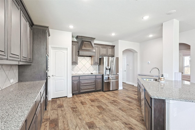 kitchen with arched walkways, premium range hood, a sink, and appliances with stainless steel finishes