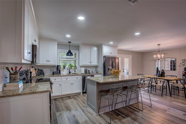 kitchen featuring appliances with stainless steel finishes, pendant lighting, light hardwood / wood-style flooring, a center island, and white cabinetry