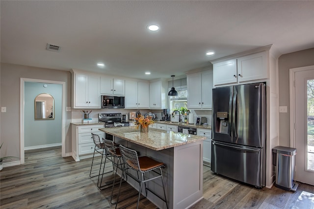 kitchen featuring white cabinets, decorative light fixtures, wood-type flooring, and stainless steel appliances