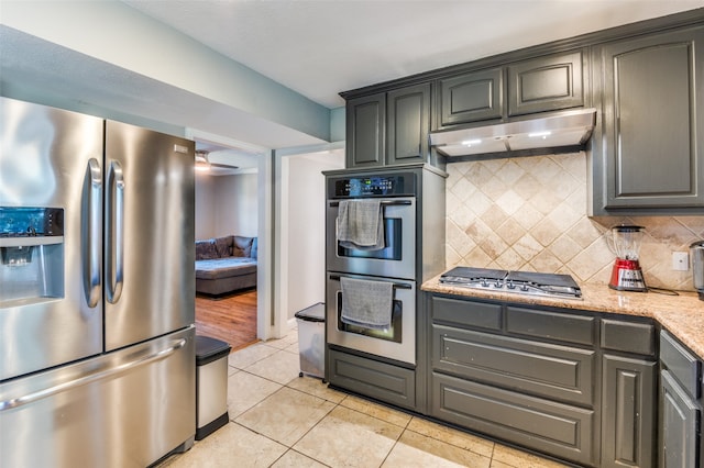 kitchen featuring decorative backsplash, stainless steel appliances, light stone countertops, and light tile patterned floors