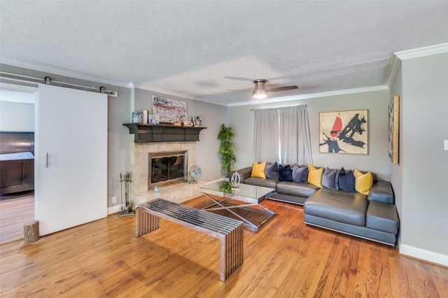 living room featuring a barn door, a textured ceiling, crown molding, ceiling fan, and light hardwood / wood-style flooring