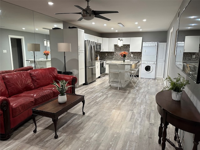 living room with light wood-type flooring, stacked washing maching and dryer, and ceiling fan