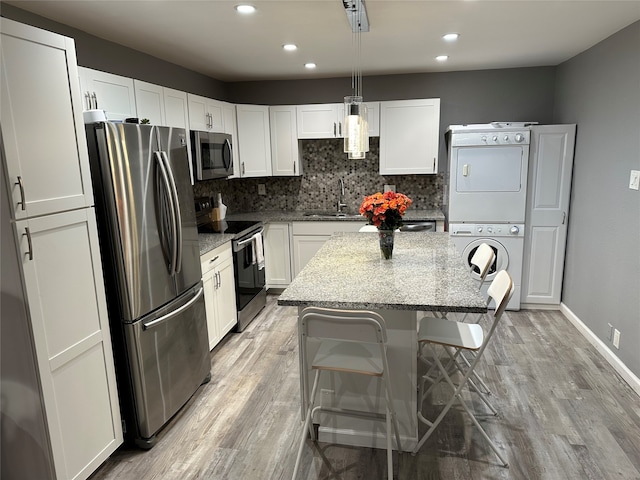 kitchen featuring appliances with stainless steel finishes, light stone counters, stacked washer and clothes dryer, a center island, and decorative light fixtures