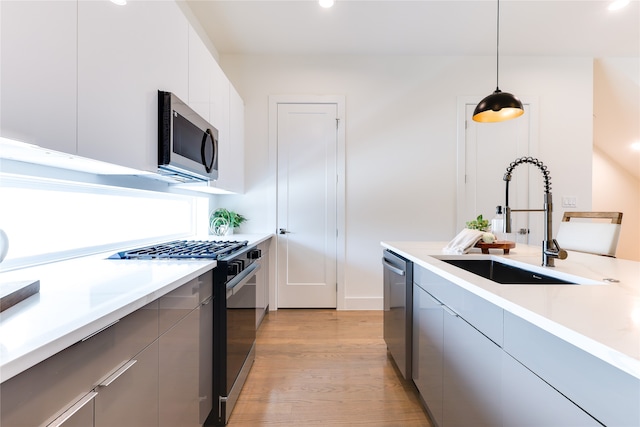 kitchen featuring decorative light fixtures, white cabinetry, sink, light hardwood / wood-style floors, and stainless steel appliances