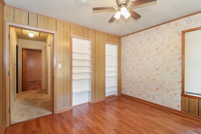 unfurnished bedroom featuring ceiling fan, hardwood / wood-style flooring, and wooden walls