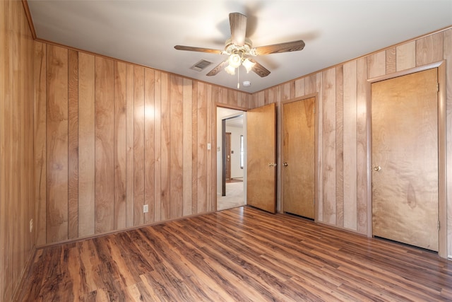 unfurnished bedroom with wooden walls, dark hardwood / wood-style flooring, and ceiling fan