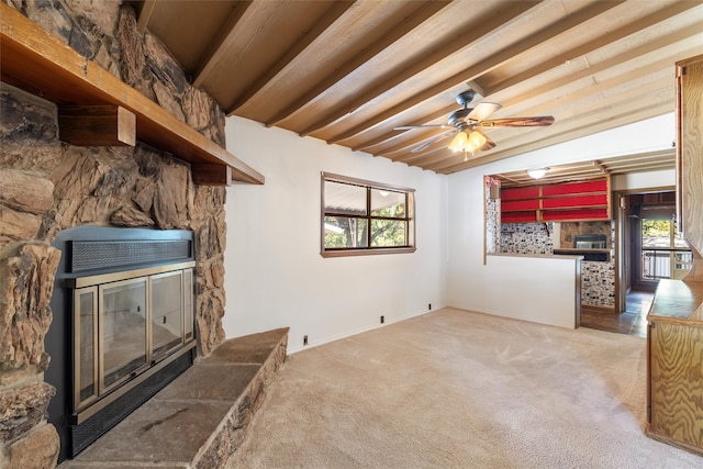 carpeted living room featuring ceiling fan, beamed ceiling, and a stone fireplace