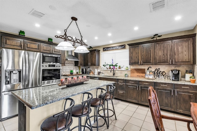 kitchen with light stone counters, light tile patterned floors, a kitchen island, decorative light fixtures, and appliances with stainless steel finishes