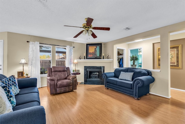 living room with wood-type flooring, a textured ceiling, a fireplace, and ceiling fan