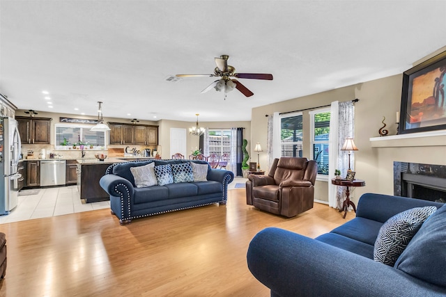 living room featuring ceiling fan with notable chandelier, light hardwood / wood-style floors, and a fireplace