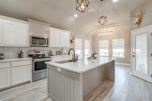 kitchen with pendant lighting, plenty of natural light, a kitchen island with sink, sink, and stainless steel appliances