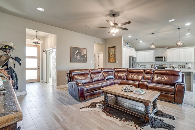 living room with a barn door, light hardwood / wood-style floors, and ceiling fan