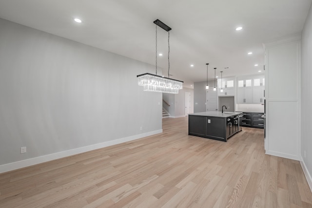 kitchen with sink, an island with sink, light hardwood / wood-style floors, pendant lighting, and white cabinets