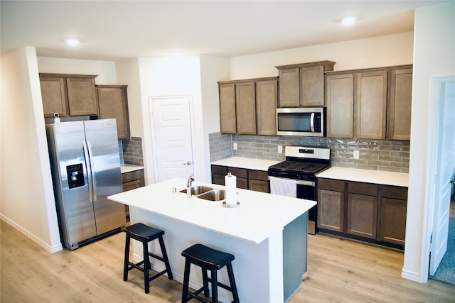 kitchen with appliances with stainless steel finishes, a kitchen breakfast bar, light hardwood / wood-style flooring, a center island with sink, and sink