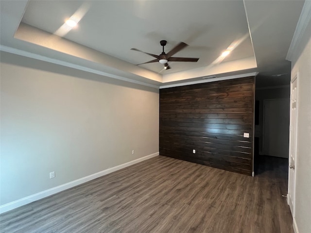 empty room with ornamental molding, ceiling fan, a raised ceiling, and dark hardwood / wood-style floors