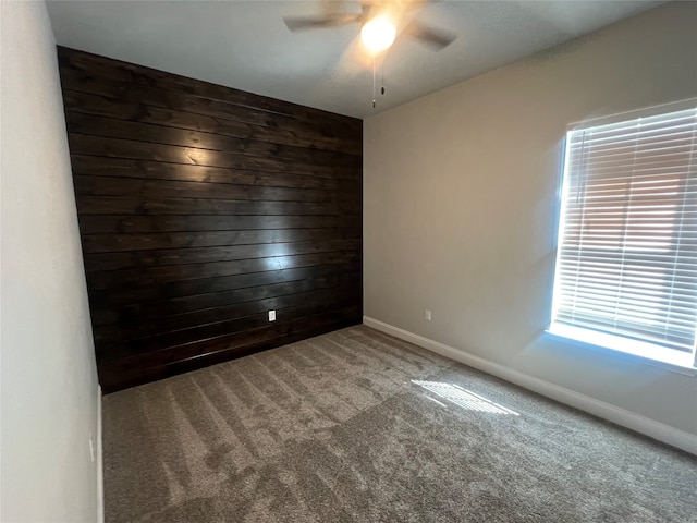 unfurnished room with ceiling fan, wooden walls, and carpet flooring