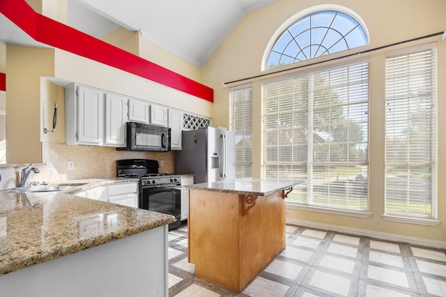 kitchen featuring white cabinets, light stone countertops, black appliances, lofted ceiling, and sink