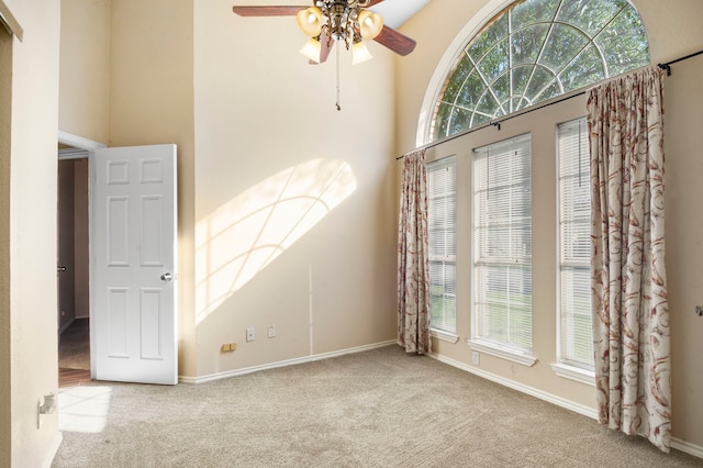 carpeted empty room with a towering ceiling and ceiling fan