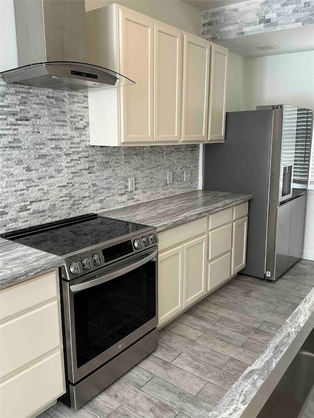 kitchen featuring appliances with stainless steel finishes, decorative backsplash, wall chimney exhaust hood, light hardwood / wood-style flooring, and cream cabinets