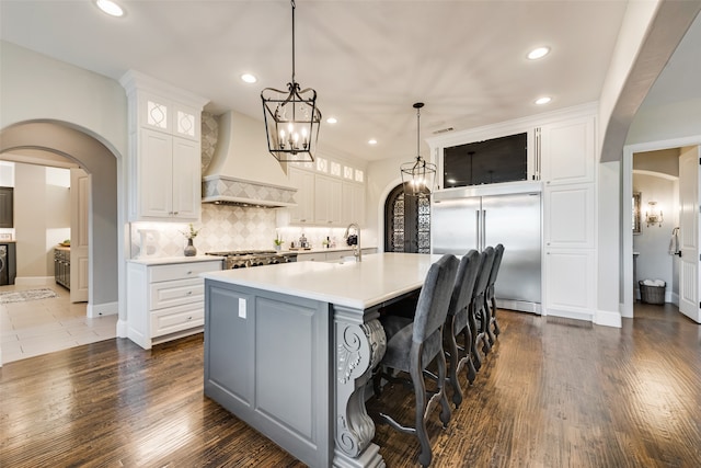 kitchen with white cabinets, custom exhaust hood, appliances with stainless steel finishes, and a large island with sink