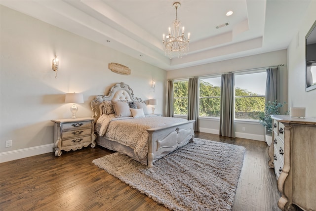 bedroom with an inviting chandelier, a raised ceiling, and dark hardwood / wood-style flooring