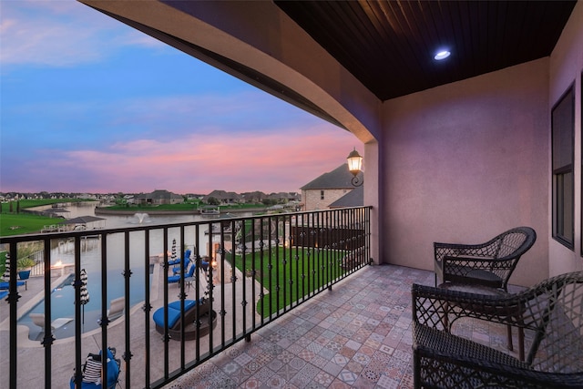 balcony at dusk featuring a water view