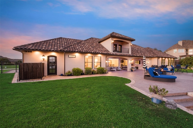 back house at dusk with a lawn, outdoor lounge area, and a patio area