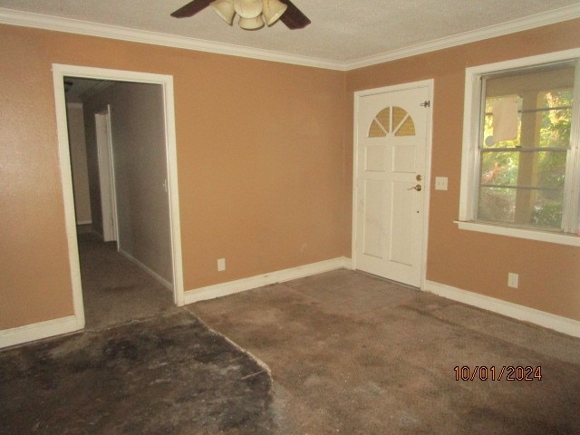 entryway featuring dark colored carpet, ceiling fan, crown molding, and a textured ceiling