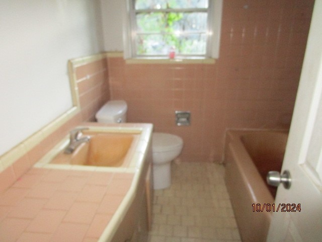 bathroom featuring tile walls, a tub to relax in, sink, and toilet