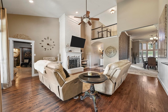 living room featuring ceiling fan with notable chandelier, a fireplace, dark hardwood / wood-style floors, and a high ceiling