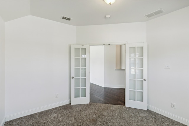 empty room featuring lofted ceiling, dark colored carpet, and french doors