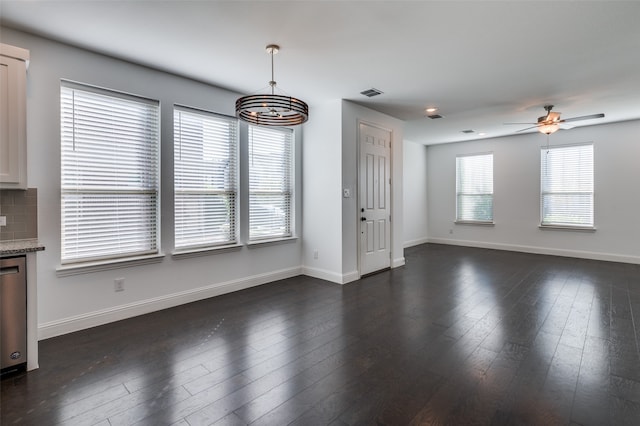 unfurnished dining area featuring ceiling fan with notable chandelier, dark hardwood / wood-style flooring, and plenty of natural light