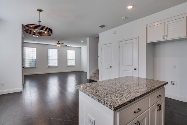 kitchen with dark wood-type flooring, white cabinetry, hanging light fixtures, a kitchen island, and light stone countertops