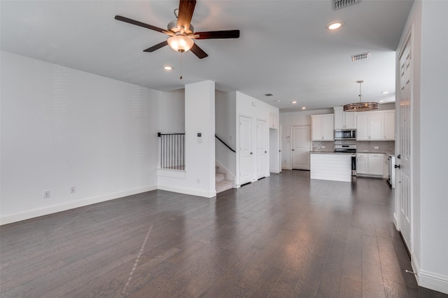unfurnished living room with dark wood-type flooring, ceiling fan, visible vents, and stairway