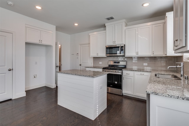 kitchen with appliances with stainless steel finishes, white cabinets, a kitchen island, dark hardwood / wood-style floors, and sink