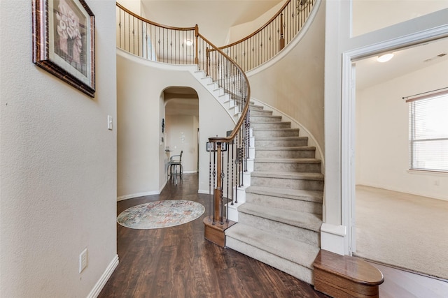 foyer entrance featuring a towering ceiling and dark wood-type flooring