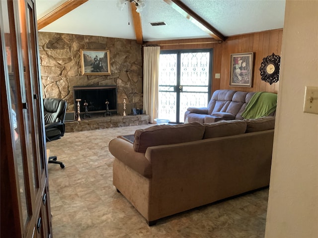 living room featuring wooden walls, beam ceiling, a textured ceiling, and a stone fireplace